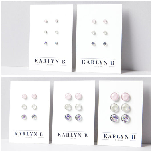 Five sets of stud earrings on white cards with the text "KARLYN B DESIGNS". Each set features three pairs of earrings in different shades of light pink, opal white and opal silver glitter.