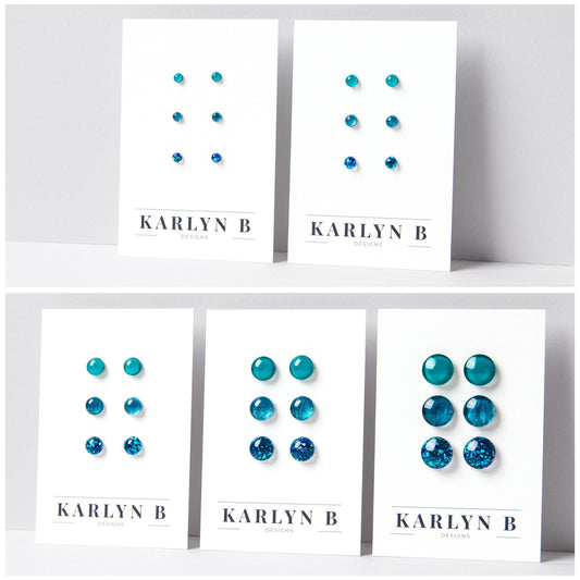 Five sets of stud earrings on white cards with the text "KARLYN B DESIGNS". Each set features three pairs of earrings in different shades of teal.