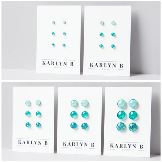 Five sets of stud earrings on white cards with the text "KARLYN B DESIGNS". Each set features three pairs of earrings in different shades of aquamarine.
