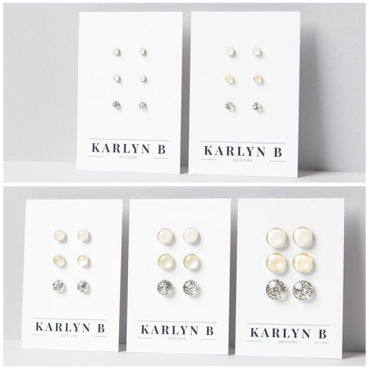 Five sets of stud earrings on white cards with the text "KARLYN B DESIGNS". Each set features three pairs of earrings in different shades of off white and ivory.