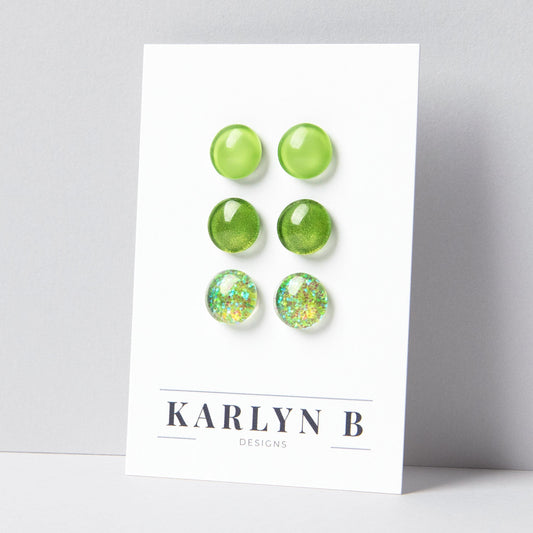 Set of three stud earrings in three different finishes - solid, shimmer, and glitter. The earrings are bright green solid, green shimmer, and green glitter. The earrings are displayed on a white card with the text "KARLYN B DESIGNS".