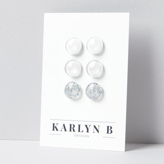 Set of three stud earrings in three different finishes - solid, shimmer, and glitter. The earrings are white solid, white shimmer, and white silver glitter. The earrings are displayed on a white card with the text "KARLYN B DESIGNS".