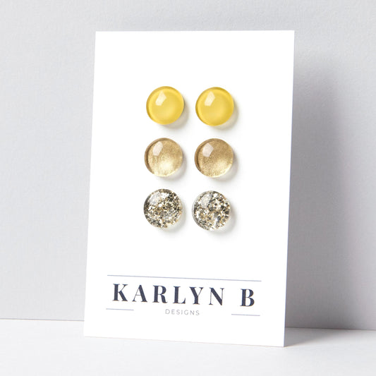 Set of three stud earrings in three different finishes - solid, shimmer, and glitter. The earrings are warm yellow, gold shimmer, and gold glitter. The earrings are displayed on a white card with the text "KARLYN B DESIGNS".