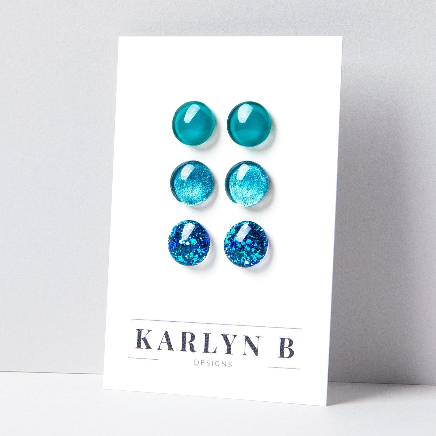 Set of three stud earrings in three different finishes - solid, shimmer, and glitter. The earrings are various shades of teal. The earrings are displayed on a white card with the text "KARLYN B DESIGNS".