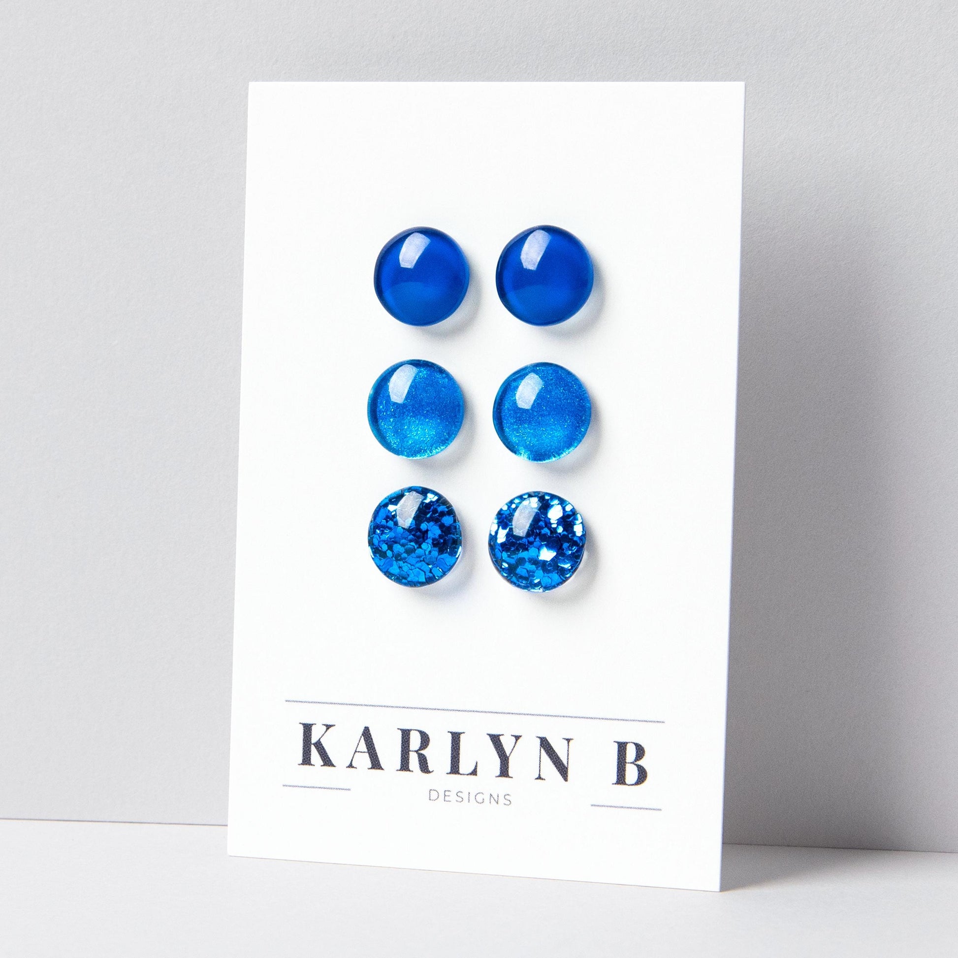 Set of three stud earrings in three different finishes - solid, shimmer, and glitter. The earrings are various shades of blue. The earrings are displayed on a white card with the text "KARLYN B DESIGNS".