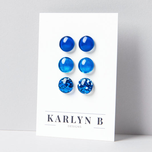 Set of three stud earrings in three different finishes - solid, shimmer, and glitter. The earrings are various shades of blue. The earrings are displayed on a white card with the text "KARLYN B DESIGNS".