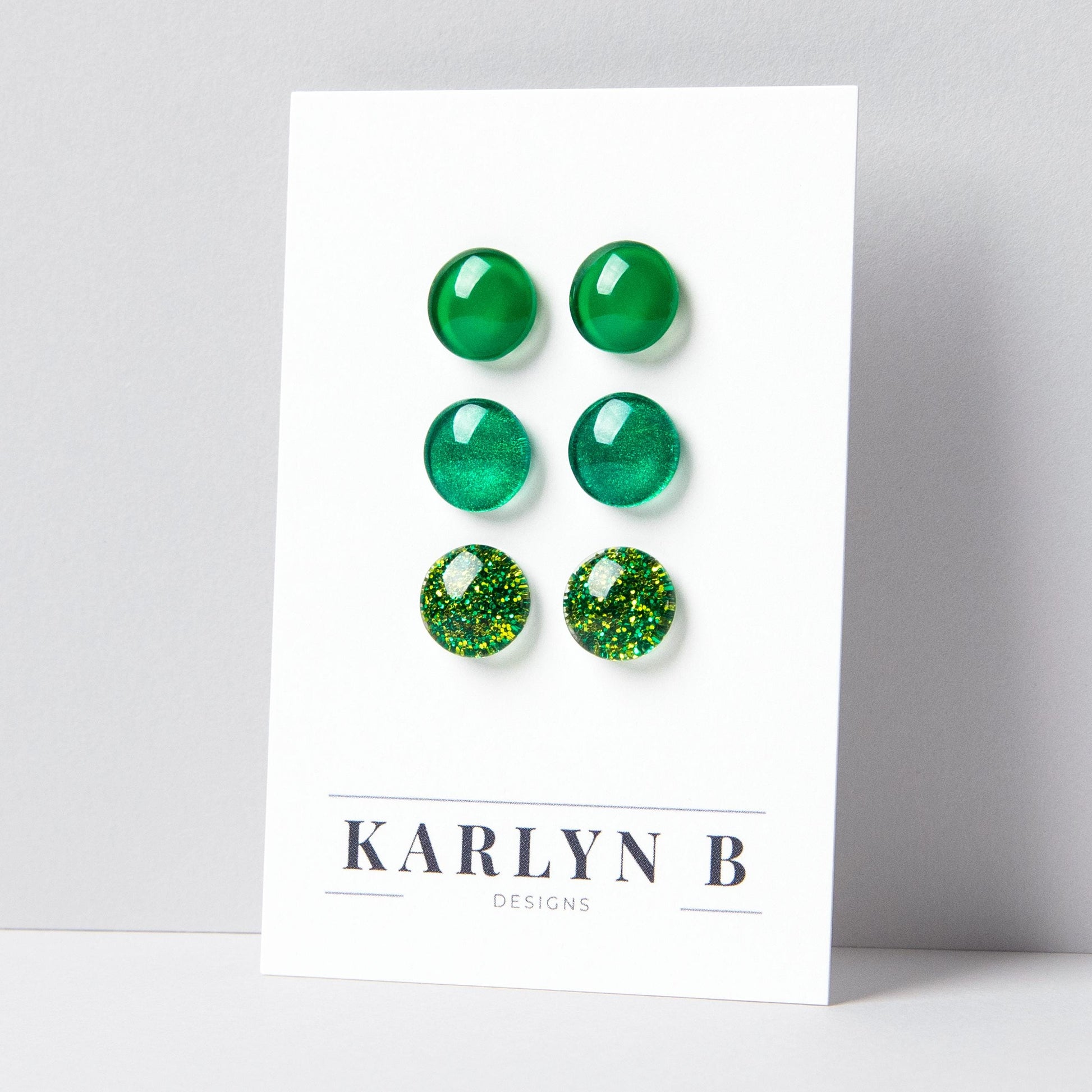 Set of three stud earrings in three different finishes - solid, shimmer, and glitter. The earrings are green solid, green shimmer, and green glitter. The earrings are displayed on a white card with the text "KARLYN B DESIGNS".