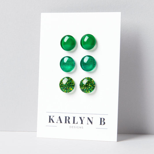 Set of three stud earrings in three different finishes - solid, shimmer, and glitter. The earrings are green solid, green shimmer, and green glitter. The earrings are displayed on a white card with the text "KARLYN B DESIGNS".