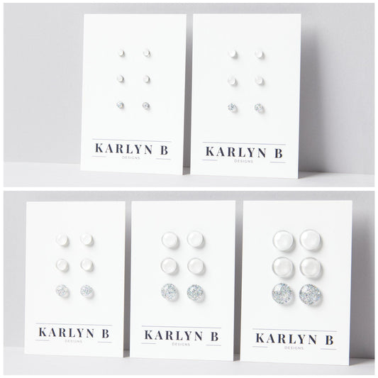 Five sets of stud earrings on white cards with the text "KARLYN B DESIGNS". Each set features three pairs of earrings in different shades of white.