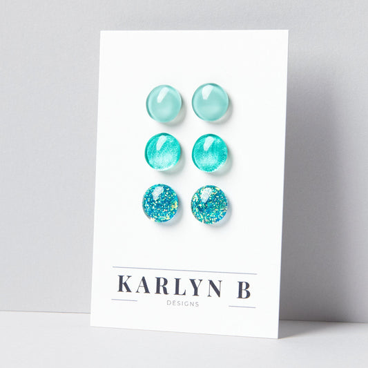 Set of three stud earrings in three different finishes - solid, shimmer, and glitter. The earrings are various shades of aquamarine. The earrings are displayed on a white card with the text "KARLYN B DESIGNS".