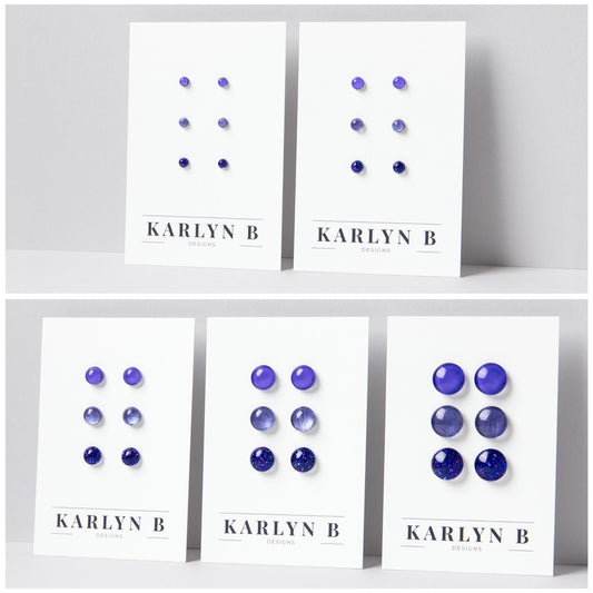 Five sets of stud earrings on white cards with the text "KARLYN B DESIGNS". Each set features three pairs of earrings in different shades of purple.