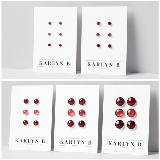 Five sets of stud earrings on white cards with the text "KARLYN B DESIGNS". Each set features three pairs of earrings in different shades of dark red.